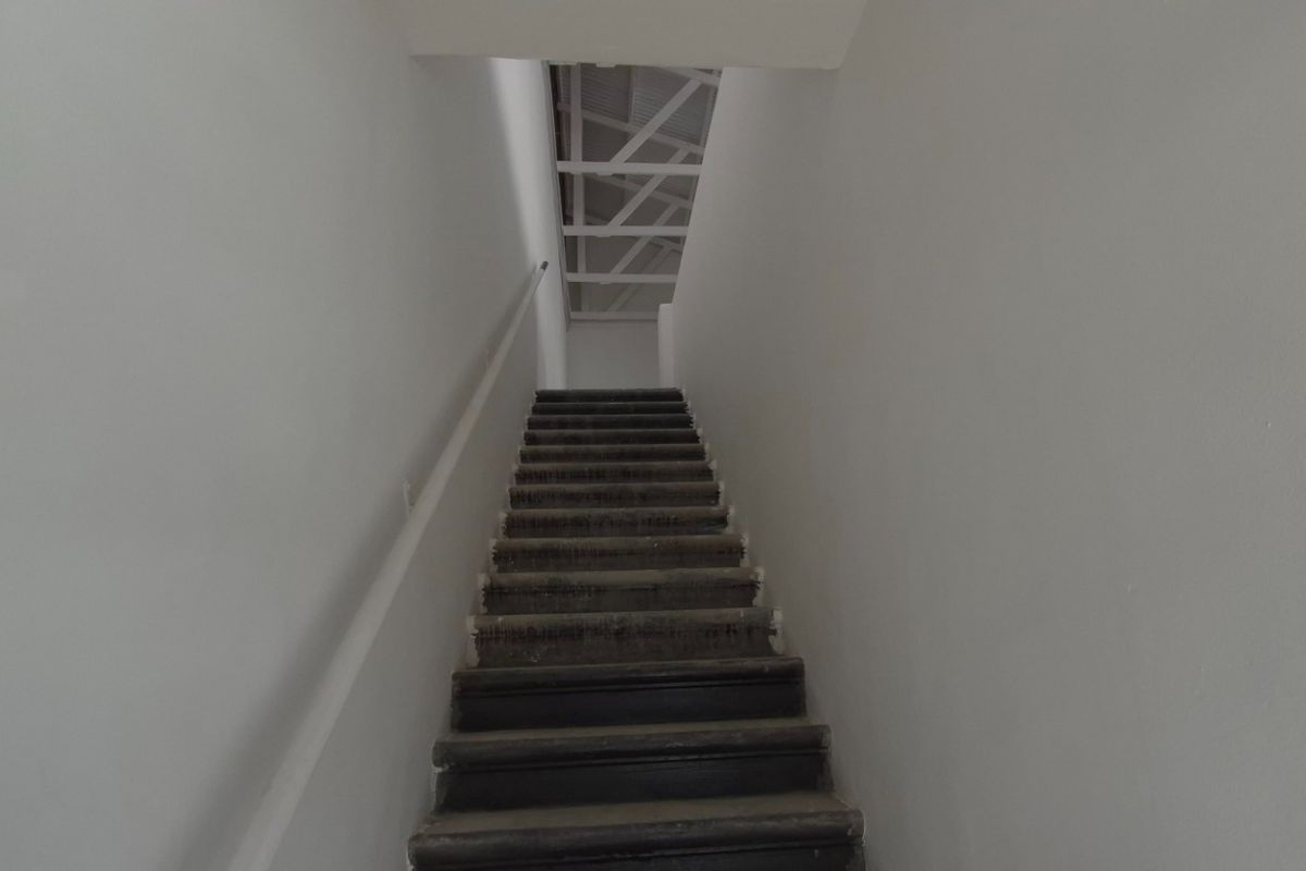 A narrow interior staircase leading to an upper level with exposed roof trusses and plain white walls.