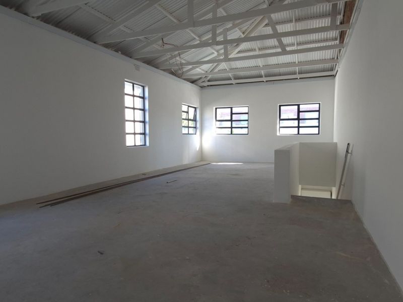 Spacious open-plan retail or office area featuring exposed roof trusses, industrial-style windows, and concrete flooring, offering a versatile blank canvas.
