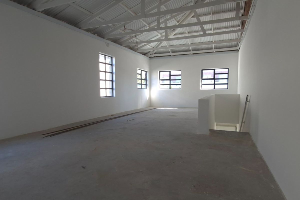 Spacious open-plan retail or office area featuring exposed roof trusses, industrial-style windows, and concrete flooring, offering a versatile blank canvas.