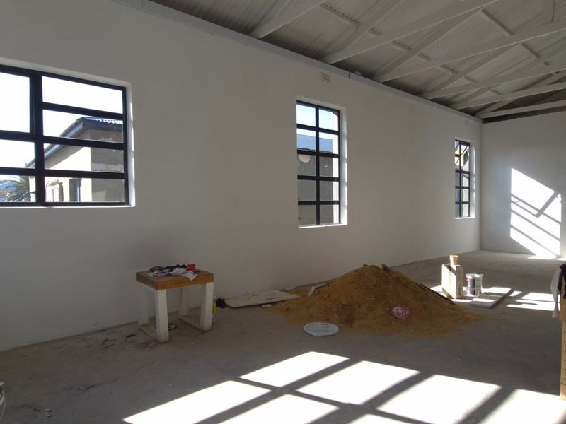 Spacious open-plan retail area featuring exposed roof trusses, large aluminium windows, and unfinished concrete flooring, currently undergoing renovation.