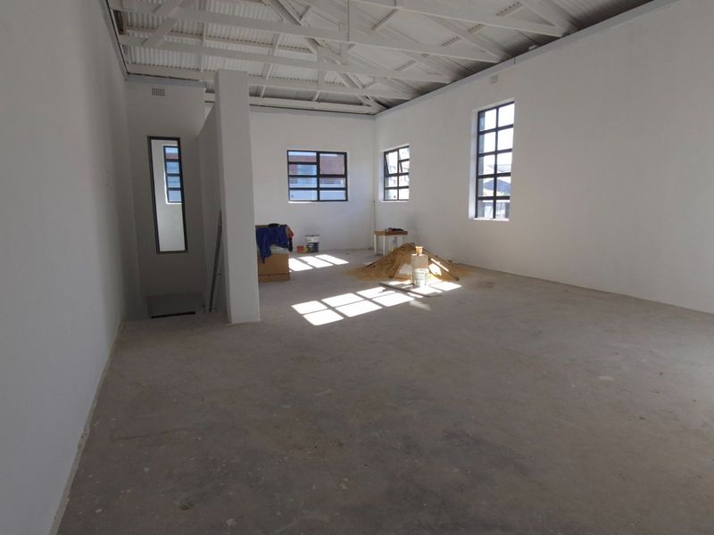 An open-plan retail space featuring exposed roof trusses, large steel-framed windows, and unfinished concrete flooring, currently in a shell condition.