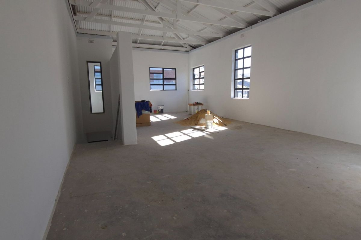 An open-plan retail space featuring exposed roof trusses, large steel-framed windows, and unfinished concrete flooring, currently in a shell condition.