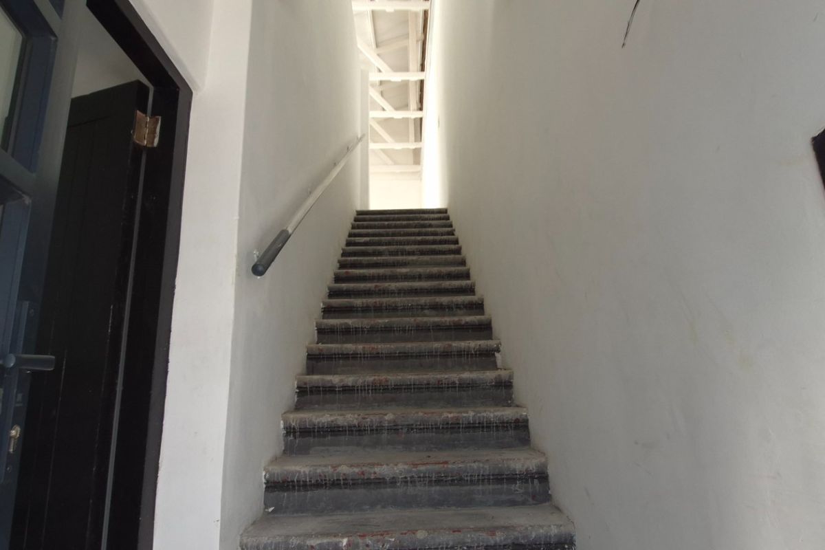A functional staircase area featuring a handrail and exposed roof trusses, currently in an unfinished state awaiting final flooring and cosmetic finishes.
