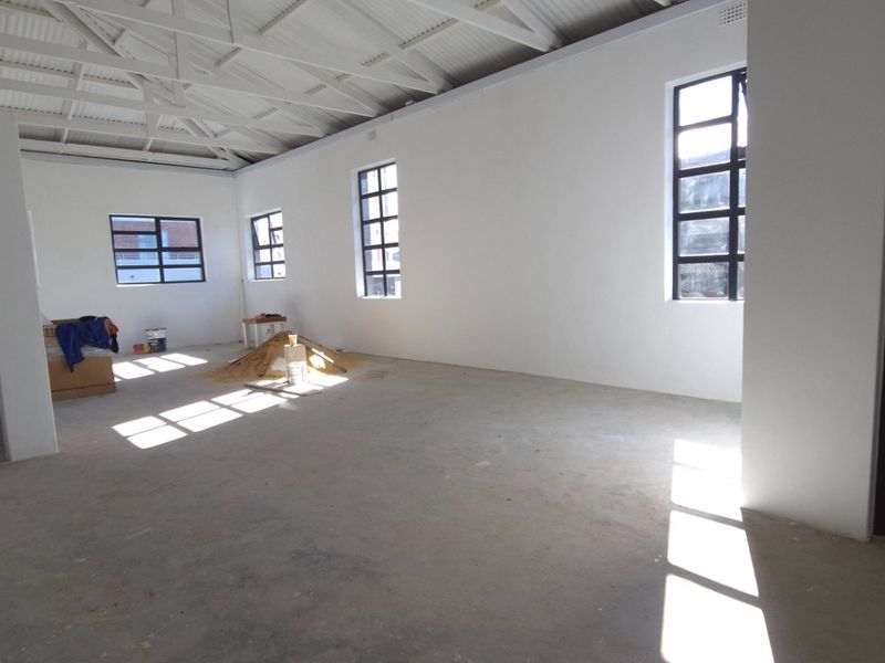 Spacious open-plan retail area featuring exposed roof trusses, concrete flooring, and large grid-style windows providing ample natural light.