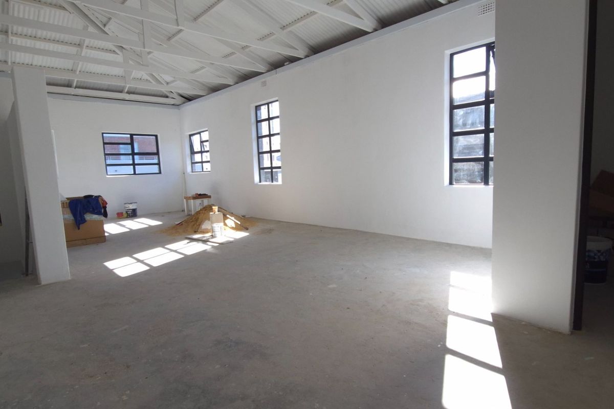 Spacious open-plan retail area featuring exposed roof trusses, concrete flooring, and large grid-style windows providing ample natural light.