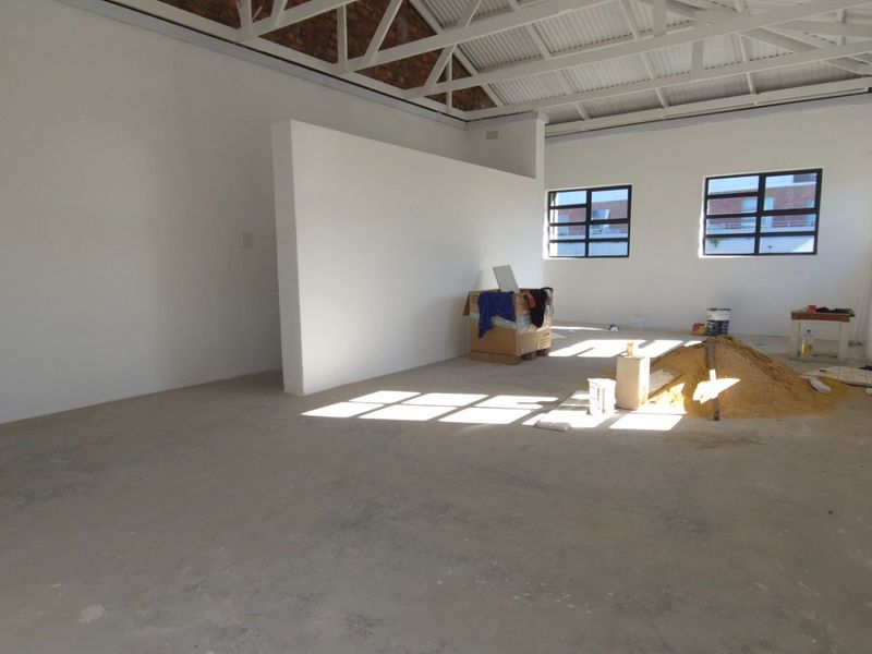 An open-plan retail space featuring exposed steel roof trusses, industrial-style windows, and concrete flooring, currently in an unfinished state.