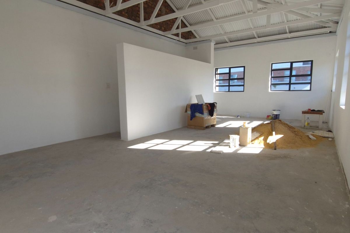 An open-plan retail space featuring exposed steel roof trusses, industrial-style windows, and concrete flooring, currently in an unfinished state.