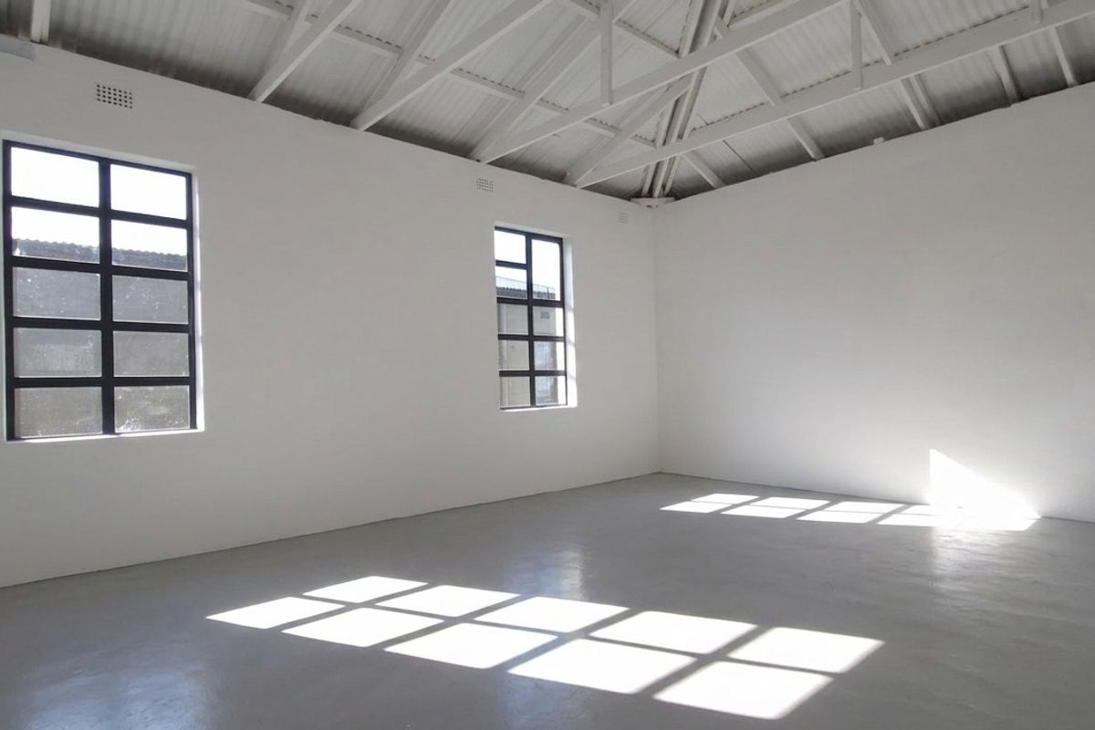 A bright, open-plan interior space featuring high ceilings with exposed white roof trusses, large steel-framed windows, and clean, painted concrete flooring.