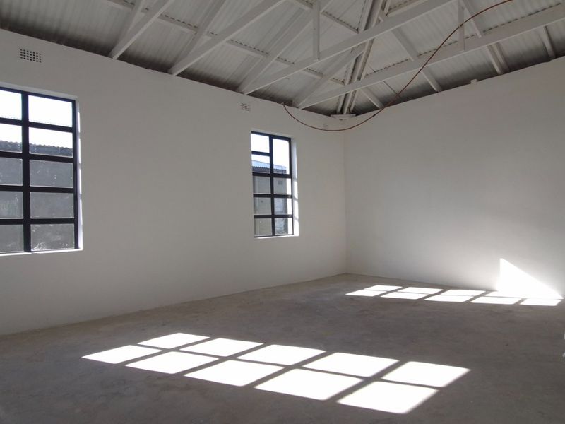 An empty, unfinished open-plan retail space featuring exposed roof trusses, concrete flooring, and steel-framed windows, ready for custom fit-out.