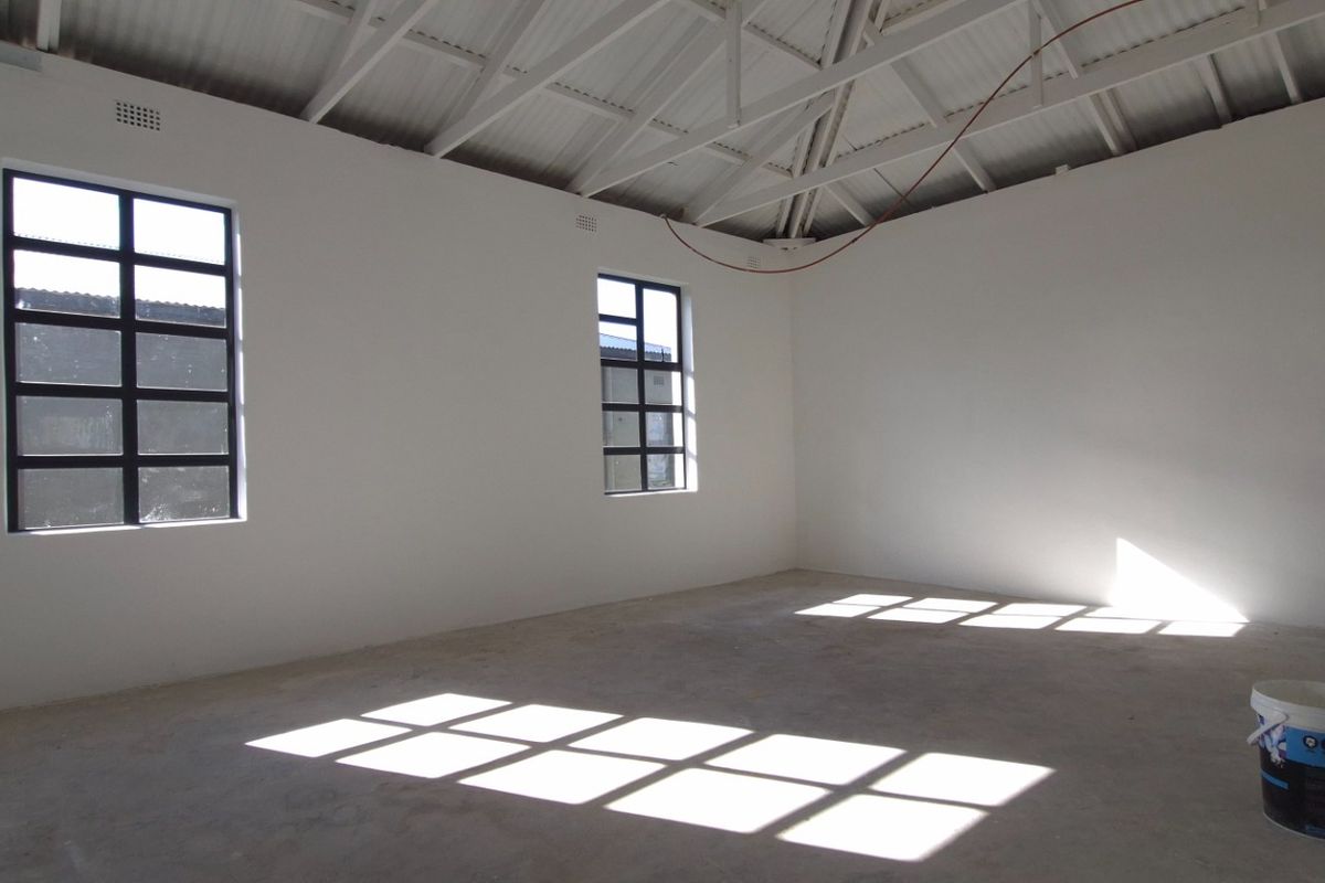 An empty, unfinished open-plan retail space featuring exposed roof trusses, concrete flooring, and steel-framed windows, ready for custom fit-out.
