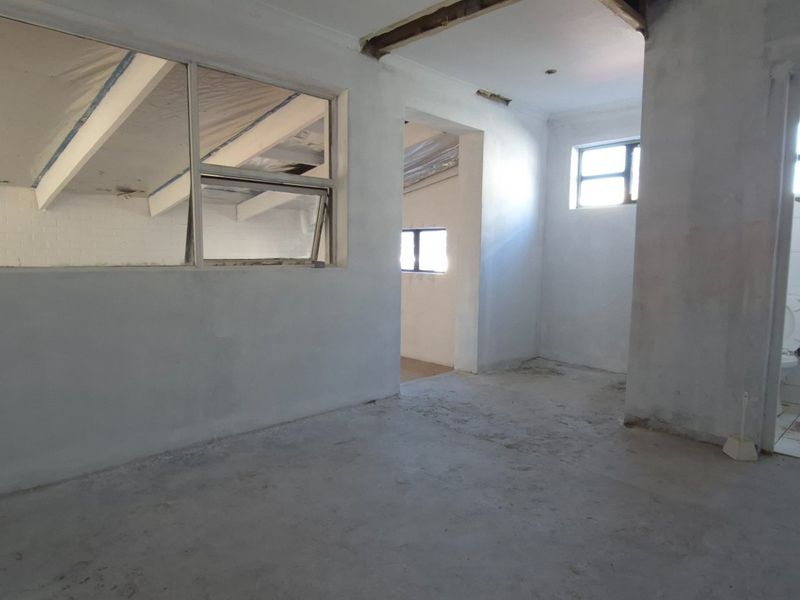 An open-plan retail or commercial space currently under renovation, featuring exposed structural elements, unfinished walls, and an adjoining bathroom area.