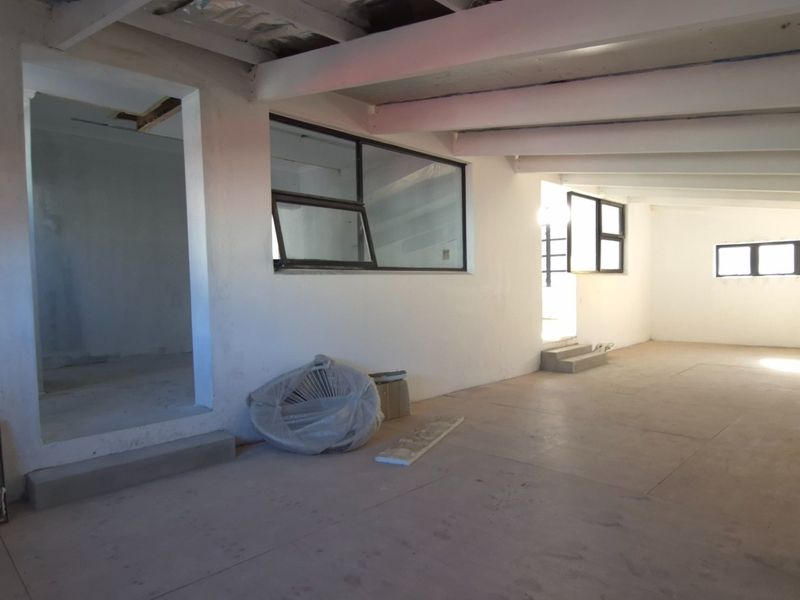 An expansive, open-plan retail space featuring exposed ceiling beams, concrete flooring, and large aluminium-framed windows, currently in a shell condition ready for fit-out.