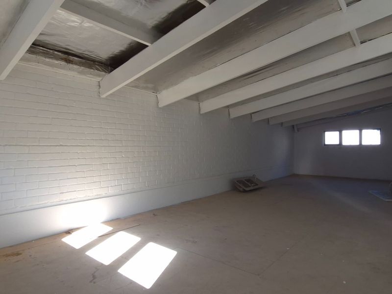 An expansive, open-plan retail space featuring exposed white-painted timber beams, painted brick walls, and unfinished concrete flooring, offering a blank canvas for customization.