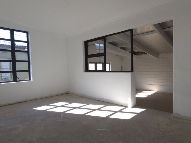 An empty, open-plan retail space featuring black-framed windows, exposed ceiling beams, and a painted brick wall, awaiting final flooring and finishing touches.