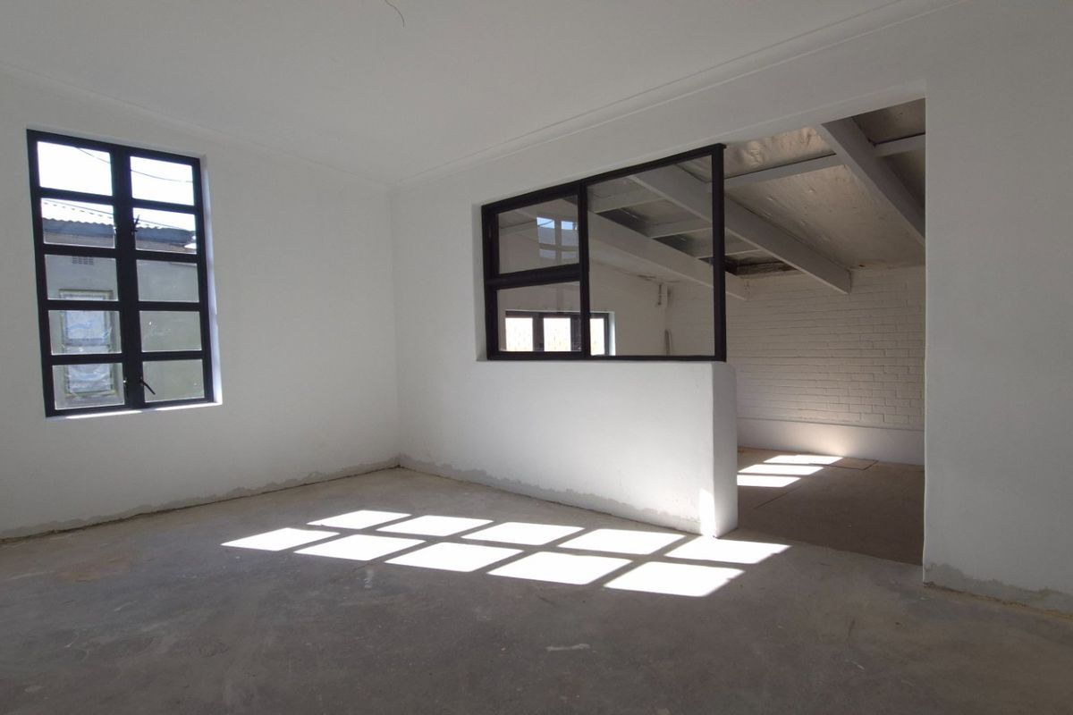An empty, open-plan retail space featuring black-framed windows, exposed ceiling beams, and a painted brick wall, awaiting final flooring and finishing touches.