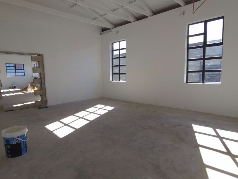 An open-plan commercial space in shell condition featuring concrete floors, exposed roof trusses, and steel-framed windows, awaiting final fit-out and finishes.