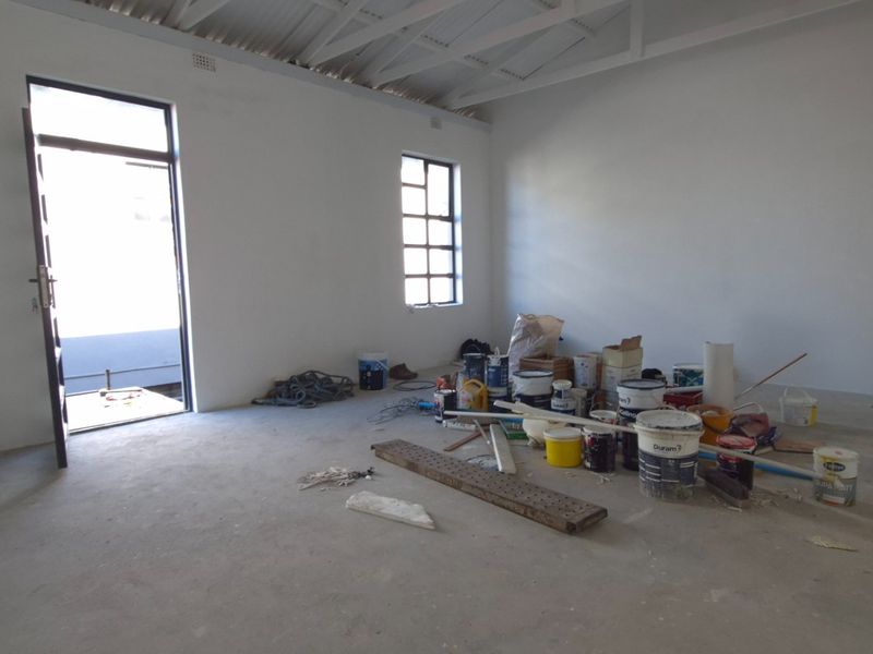 An unfinished interior space featuring exposed roof trusses, concrete flooring, and steel-framed windows, currently used for storage of construction materials.