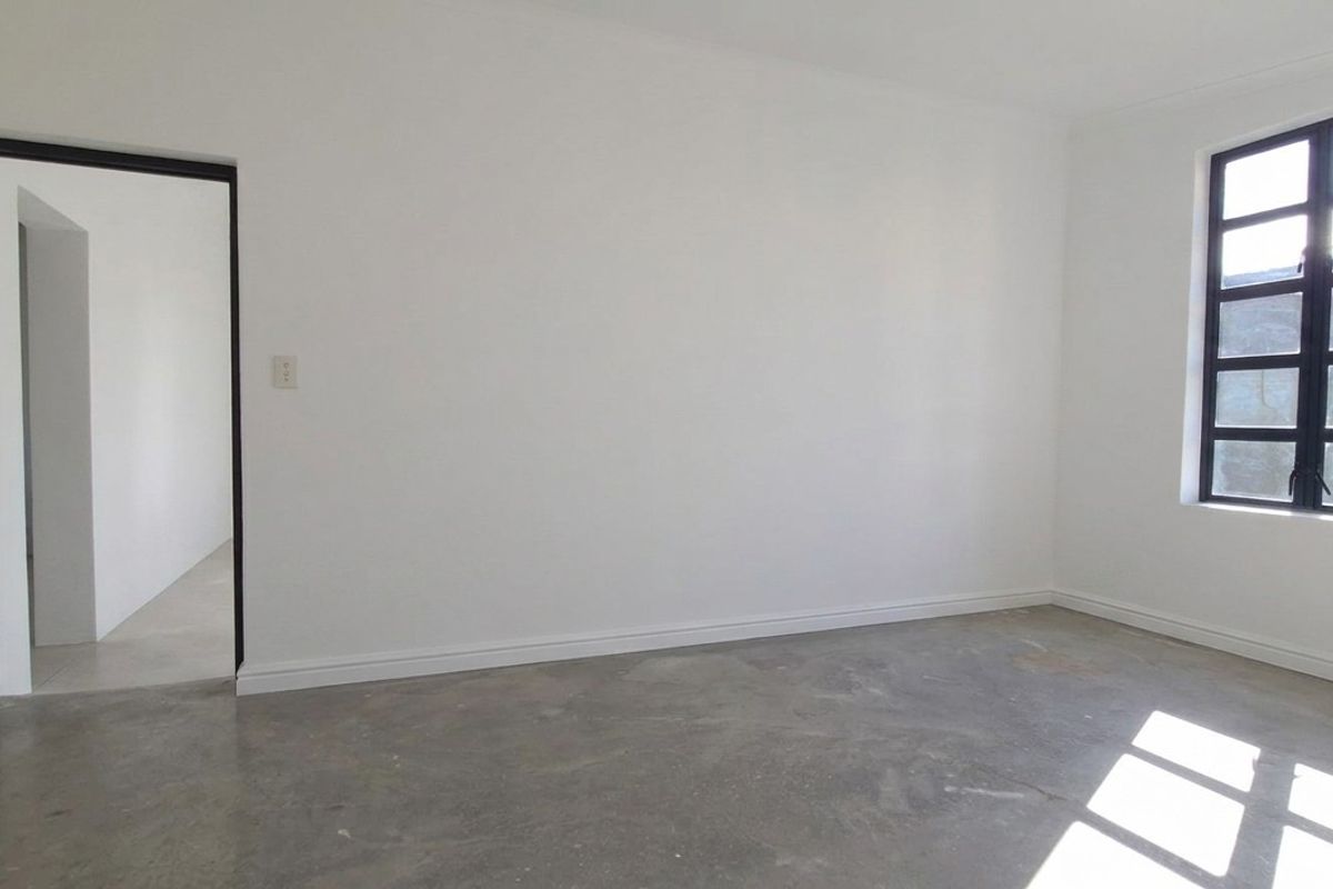 A bright, empty room featuring white walls, a black-framed window, and an unfinished concrete floor, suitable for various retail or office uses.