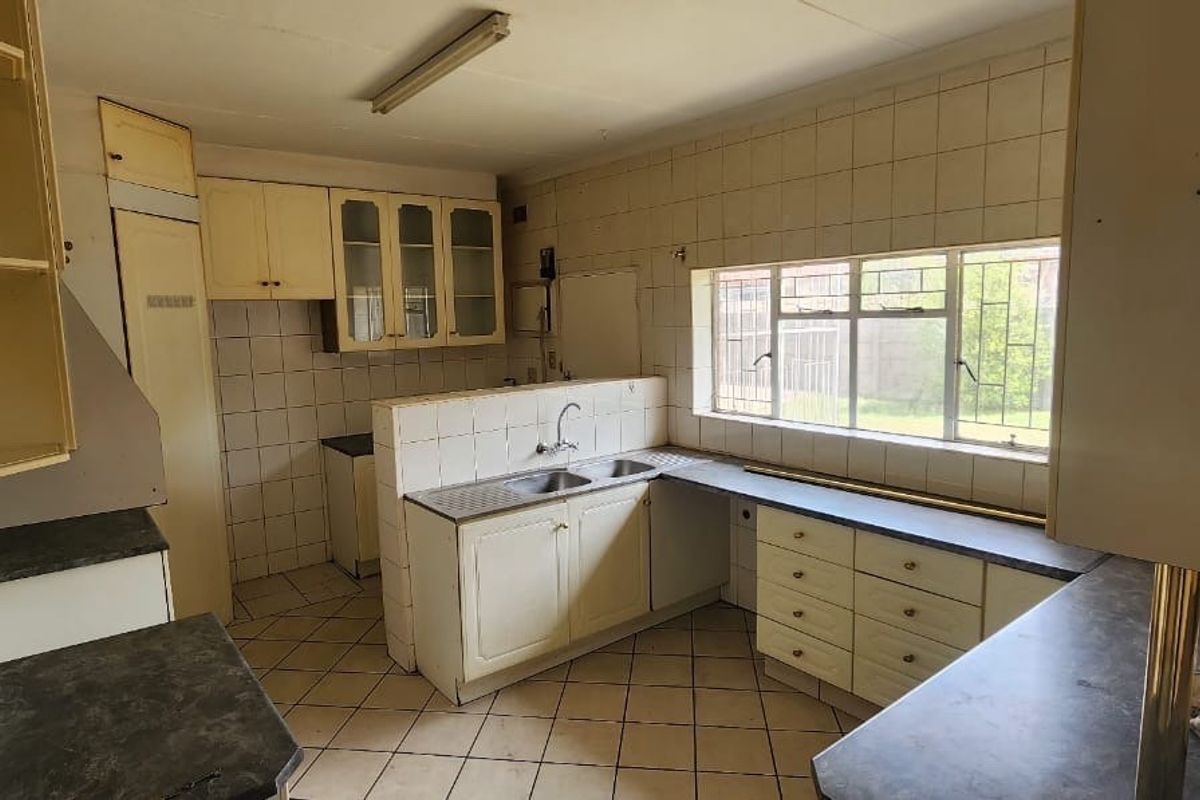 A dated kitchen featuring original cabinetry, tiled splashbacks, and a double basin sink, offering significant potential for a modern renovation.