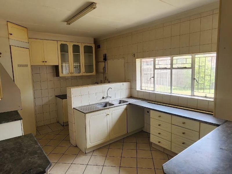 A dated kitchen featuring original cabinetry, tiled splashbacks, and a double basin sink, offering significant potential for a modern renovation.