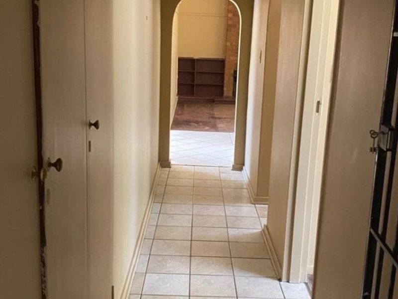 A functional hallway featuring tiled flooring and built-in storage cupboards, leading through an archway into an adjacent living space.