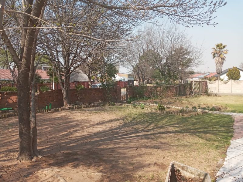 Spacious rear garden featuring mature trees, a brick boundary wall, and a paved walkway, offering potential for landscaping and outdoor improvement.