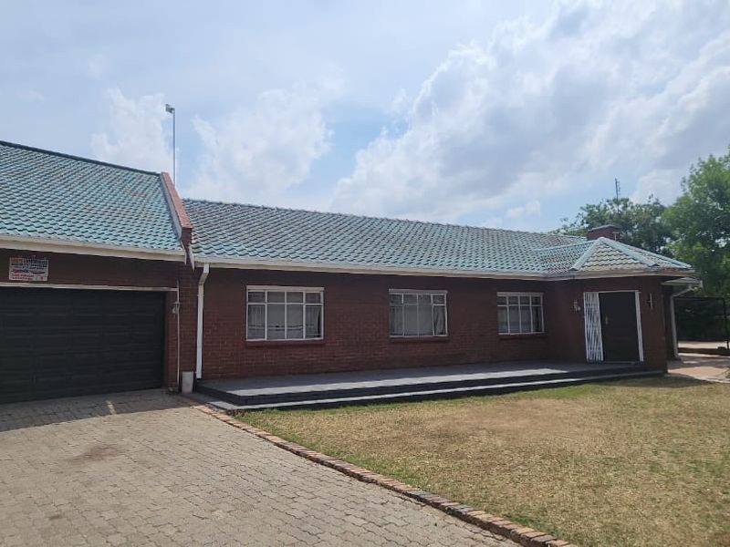 Front view of a single-story brick house featuring a tiled roof, double garage, paved driveway, and a front porch area.