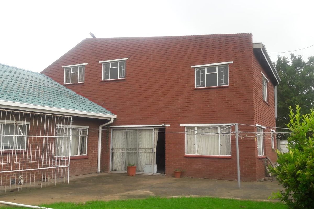 Rear view of a double-story face brick house featuring a concrete patio, sliding glass doors, and security bars on windows.