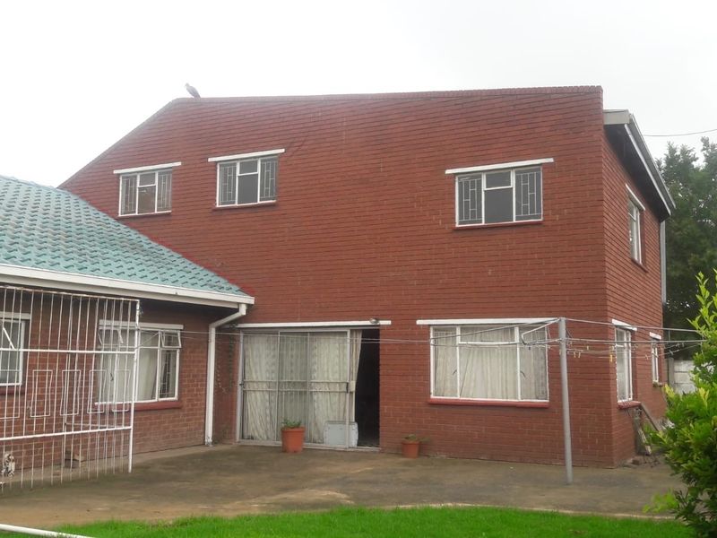 Rear view of a double-story face brick house featuring a concrete patio, sliding glass doors, and security bars on windows.