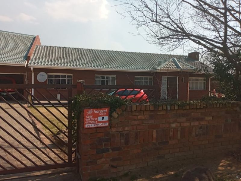 Front view of a single-story brick house featuring a tiled roof, metal driveway gate, and a brick boundary wall.