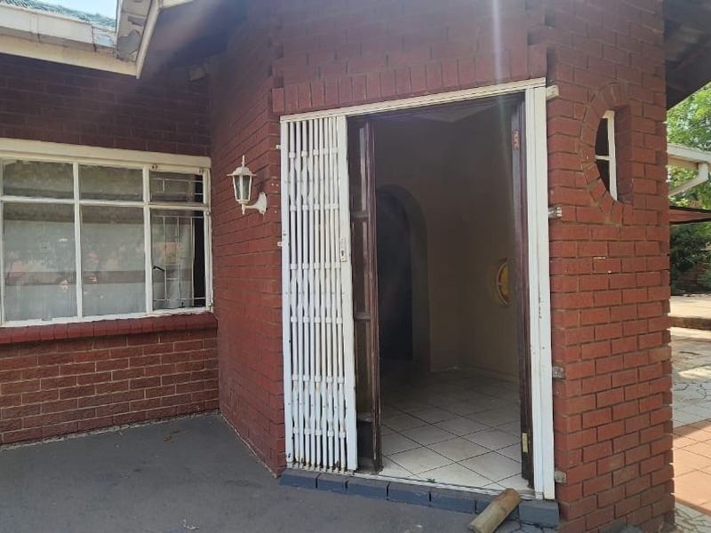 Rear exterior view of the property featuring a face brick facade, tiled patio area, and a secure entrance with a metal security gate.