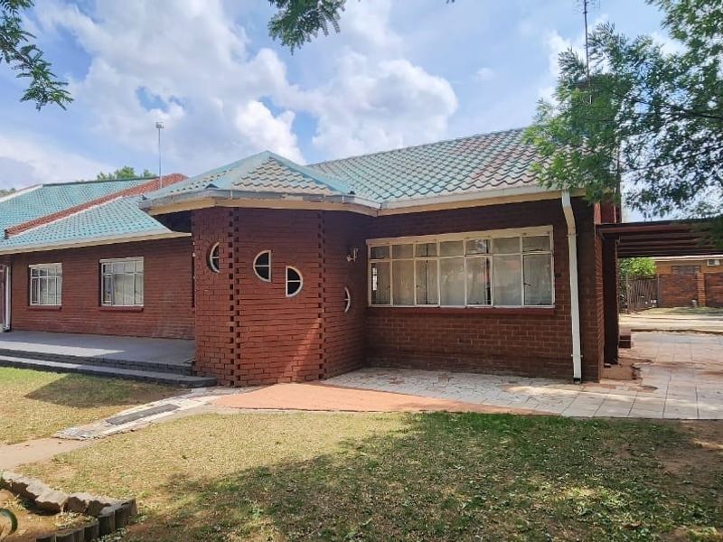 Front elevation of a face-brick house featuring a tiled roof, double garage, and an attached carport with a paved driveway and garden area.