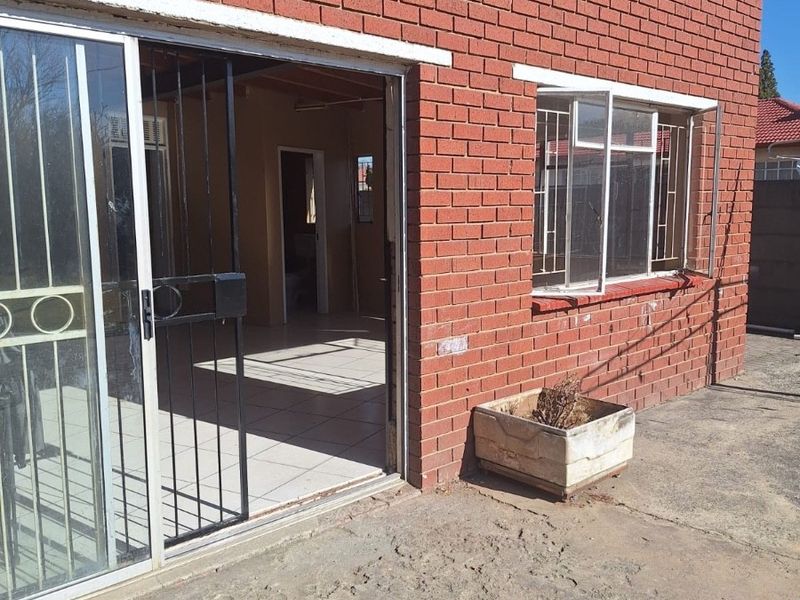 Rear exterior view of a red brick house featuring a sliding glass door with security gate and a concrete patio area.