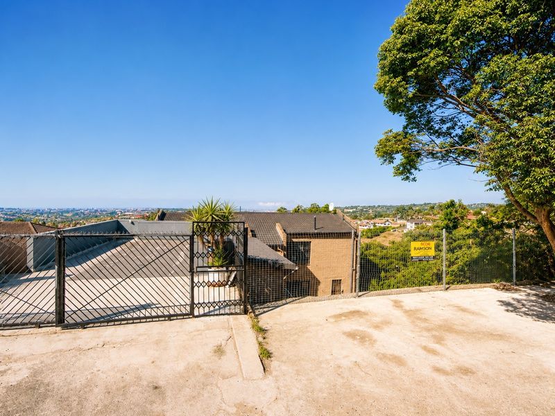 Exterior view of the property entrance featuring a concrete driveway, metal security gate, and surrounding chain link fencing with a scenic landscape view.