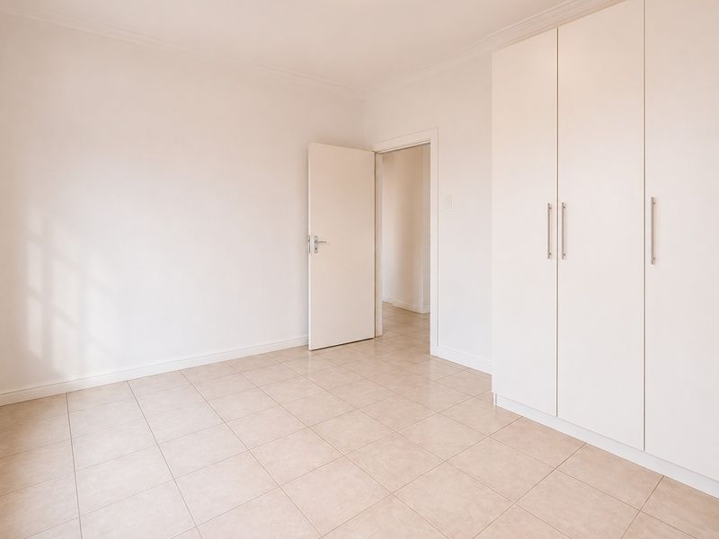 A bright, empty bedroom featuring neutral tiled flooring and ample built-in cupboard storage space.