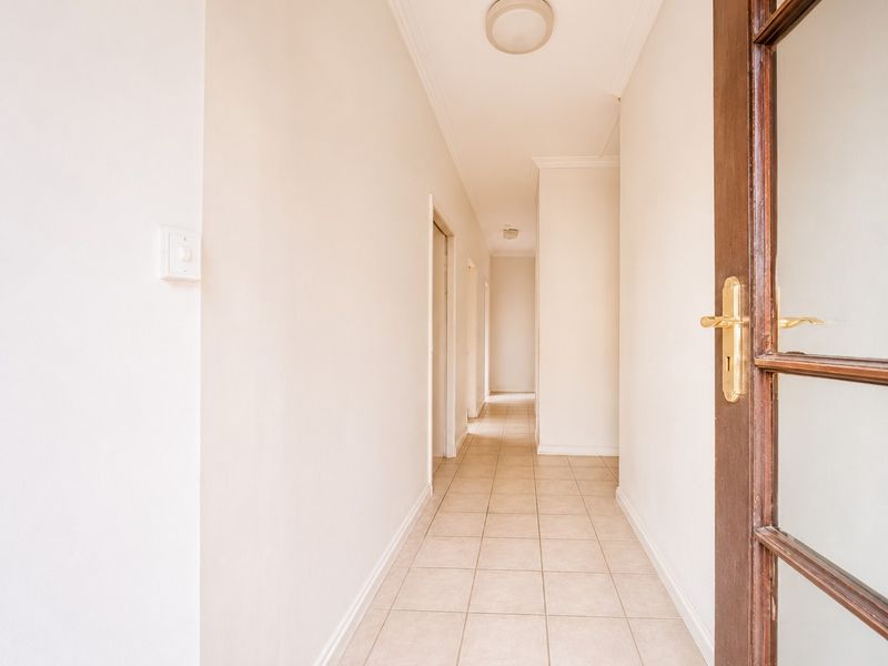 A clean and bright interior hallway featuring neutral tiled flooring, coving, and a timber-framed glass entrance door.