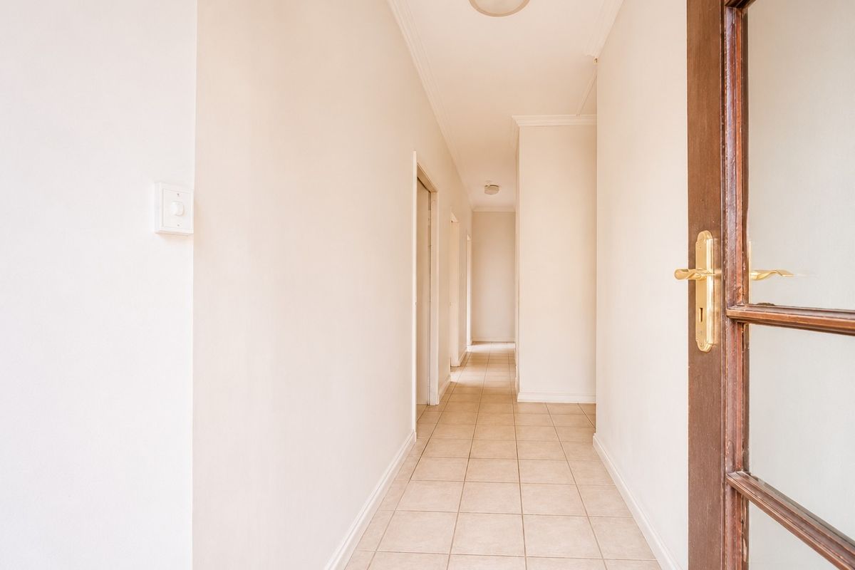 A clean and bright interior hallway featuring neutral tiled flooring, coving, and a timber-framed glass entrance door.