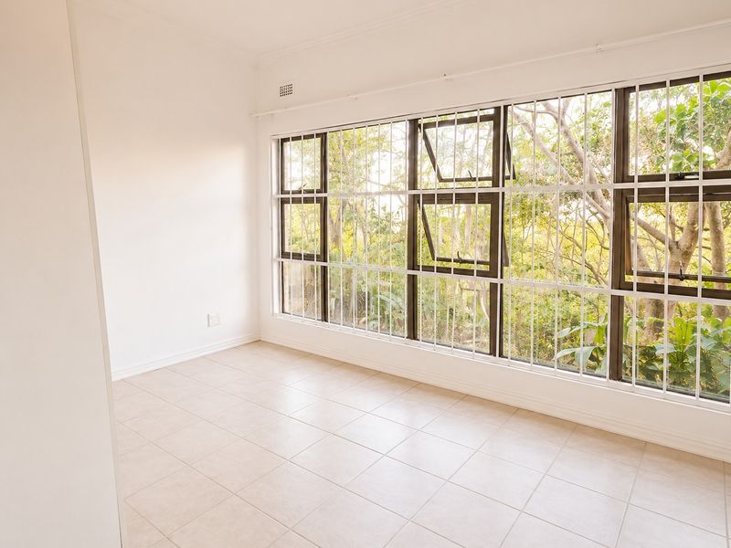 A bright, empty bedroom featuring neutral tiled flooring, large windows with security bars, and built-in storage, offering a clean canvas for personalization.