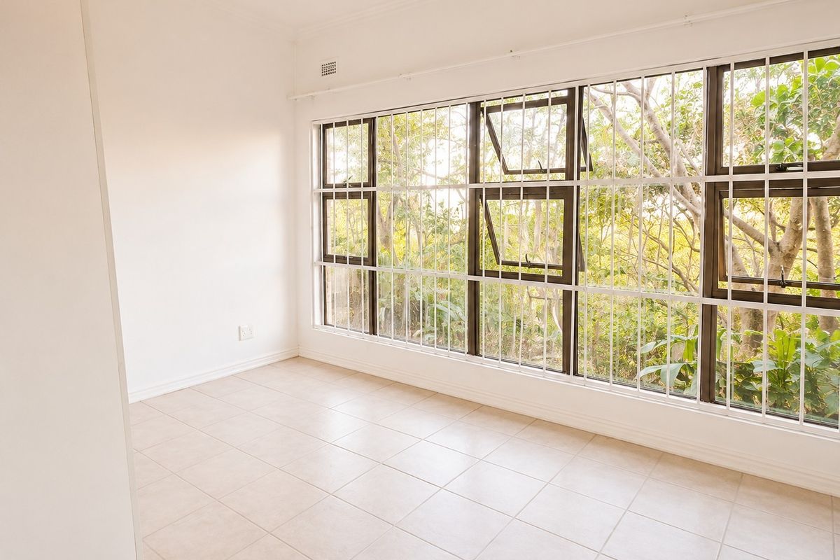 A bright, empty bedroom featuring neutral tiled flooring, large windows with security bars, and built-in storage, offering a clean canvas for personalization.