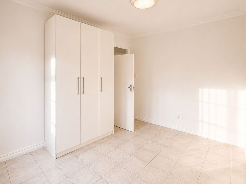 A bright, empty bedroom featuring neutral tiled flooring, a built-in white wardrobe, and clean finishes, ready for personalization.