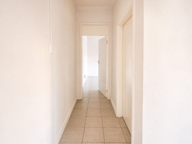 A clean, empty hallway featuring neutral tiled flooring and white walls, providing access to adjacent rooms.