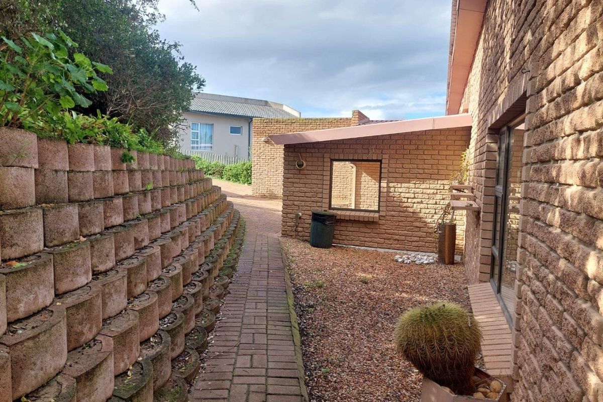 A rear exterior view featuring a brick paved pathway, a tiered retaining wall, and exposed brick building facade.
