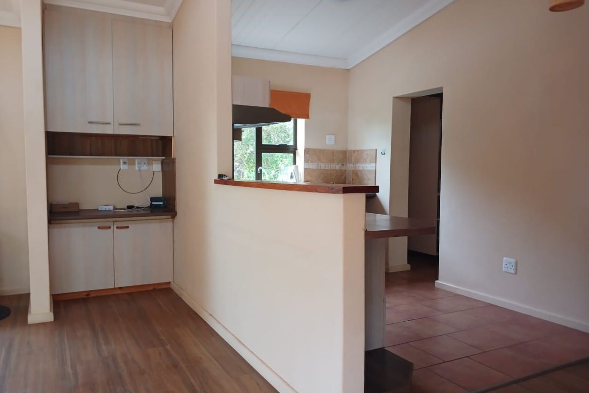 A functional kitchen area featuring built-in cabinetry, a breakfast bar, and a combination of tiled and timber flooring, offering a clean, neutral space.