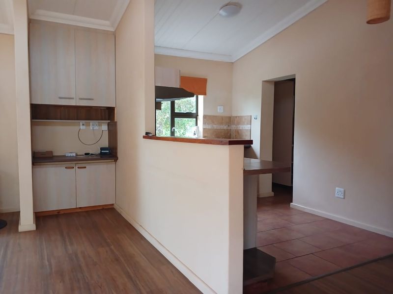 A functional kitchen area featuring built-in cabinetry, a breakfast bar, and a combination of tiled and timber flooring, offering a clean, neutral space.