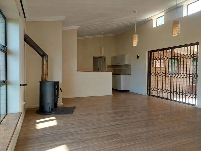 Spacious open-plan living area featuring laminate flooring, a wood-burning fireplace, and an adjoining kitchen space with built-in cabinetry and access to the patio.