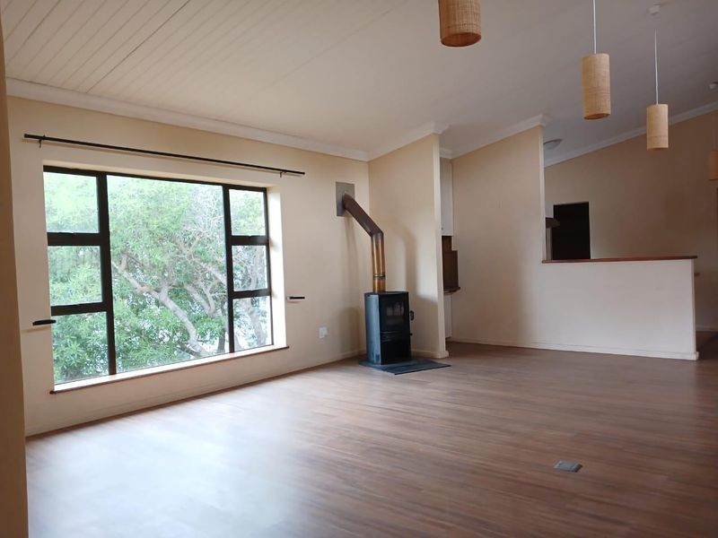 Spacious living area featuring a wood-burning fireplace, laminate flooring, and a large window providing natural light and garden views.