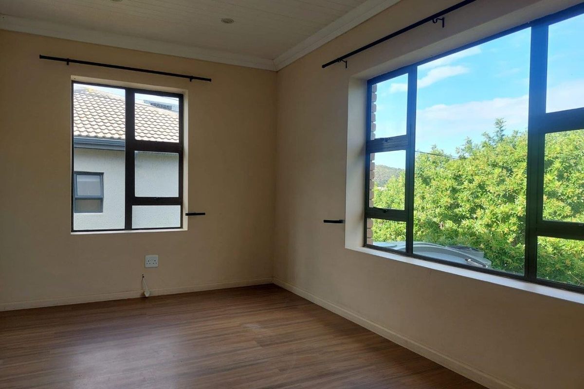A bright, empty bedroom featuring laminate flooring, aluminium window frames, and a tongue and groove ceiling with recessed lighting.