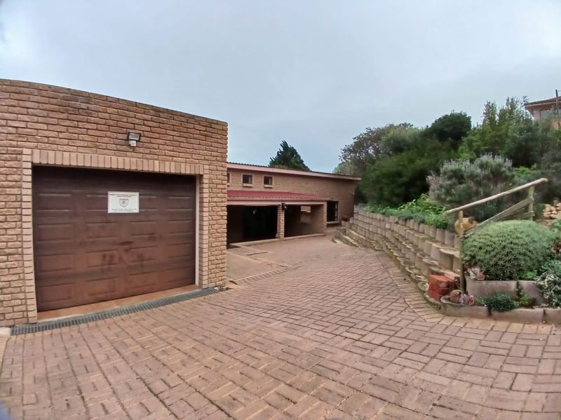 Front exterior view featuring a brick garage with a sectional door, paved driveway, and tiered retaining wall with established landscaping.