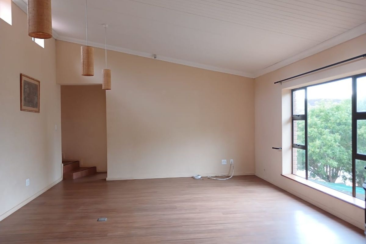 A spacious, light-filled living area featuring laminate flooring, a timber-look ceiling, and large windows with views of the surrounding greenery.