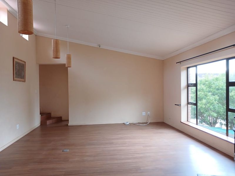 A spacious, light-filled living area featuring laminate flooring, a timber-look ceiling, and large windows with views of the surrounding greenery.